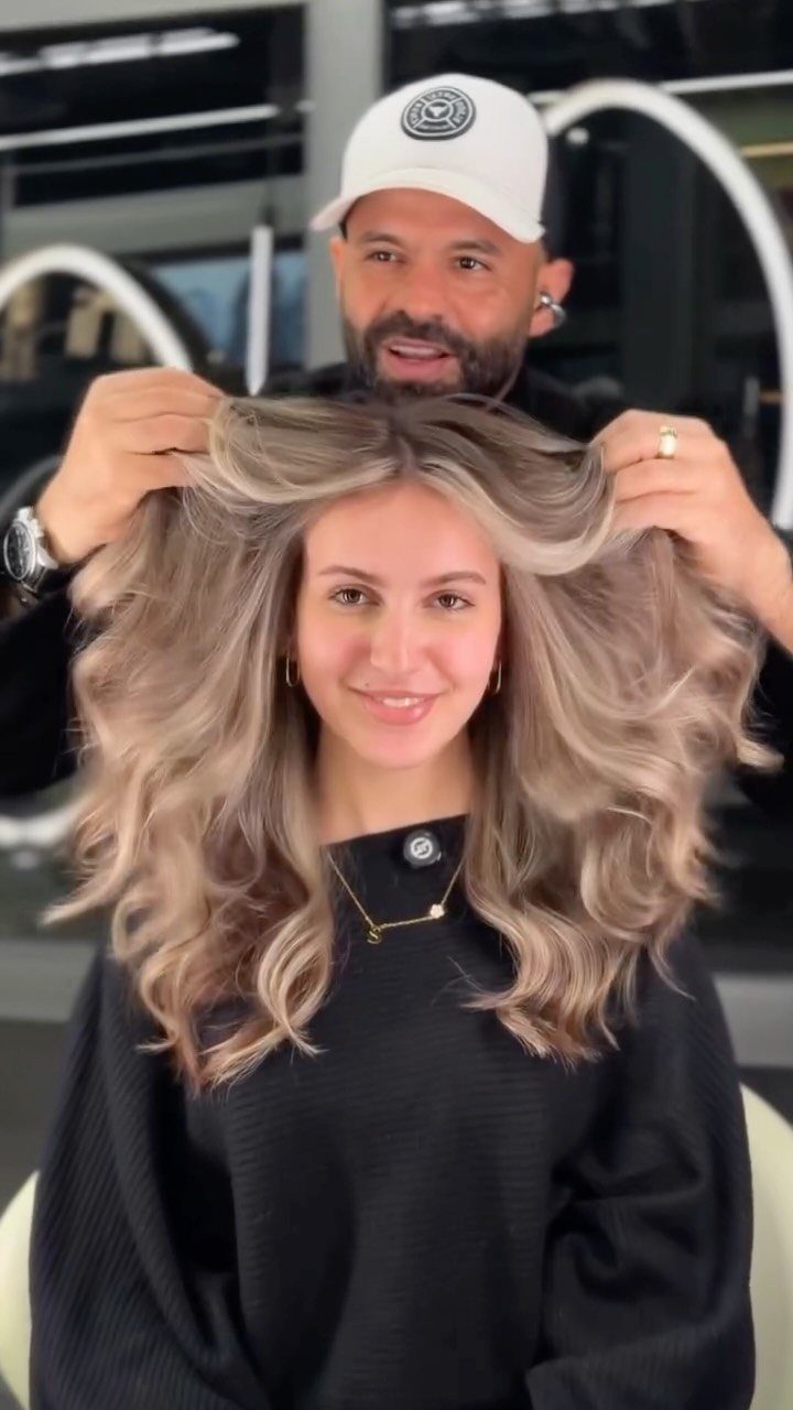 Woman with long, light blonde curls as a stylist lifts her hair