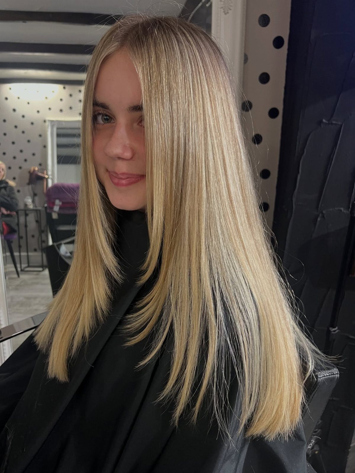 Woman displaying long, straight dirty blonde layers with darker roots in a salon