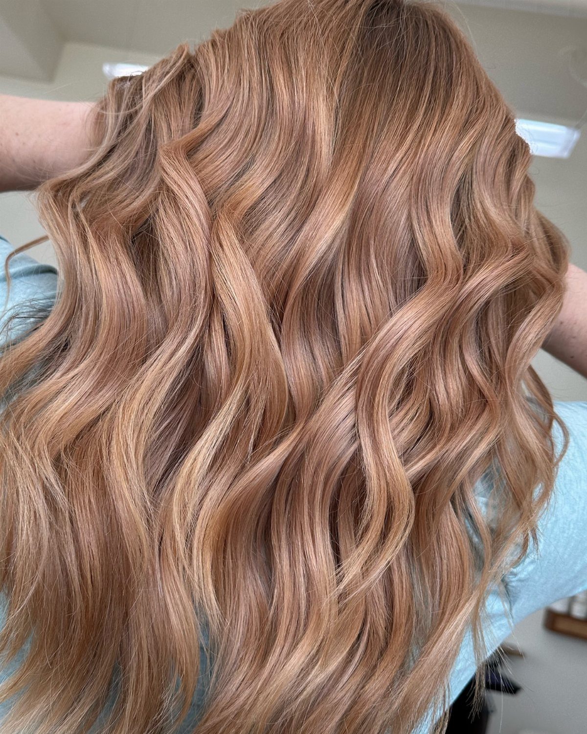 Long blonde waves with soft rose-gold highlights in a salon