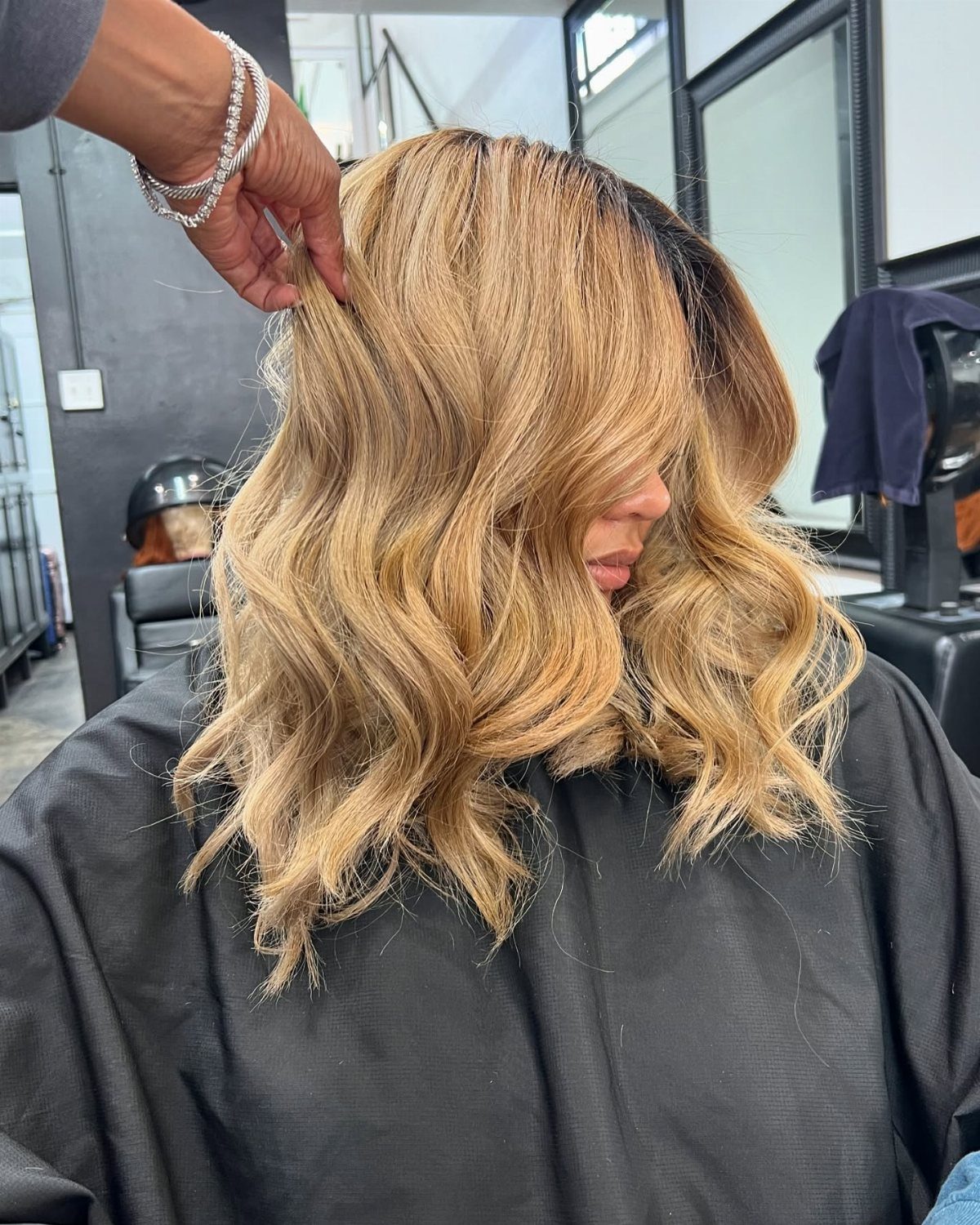 Wavy wheat-blonde hair with lighter highlights being lifted in a salon