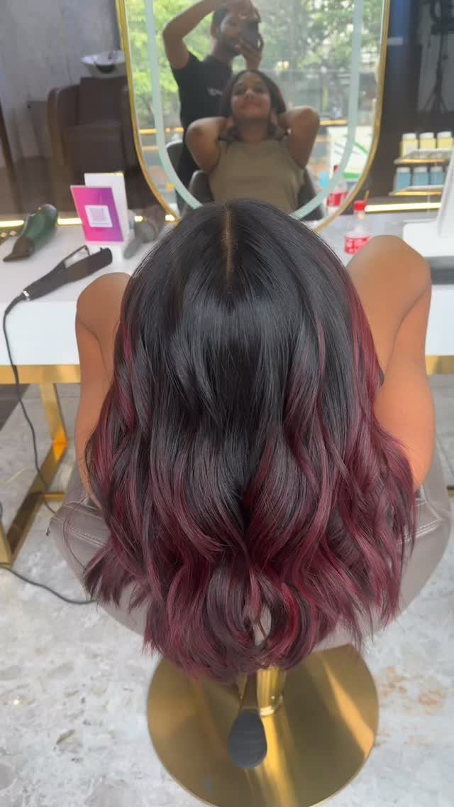 Wavy dark hair fades into burgundy-red ends in a salon chair
