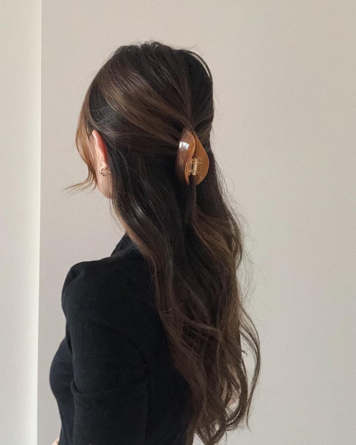 Long wavy brunette hair secured half-up with a tortoiseshell claw clip