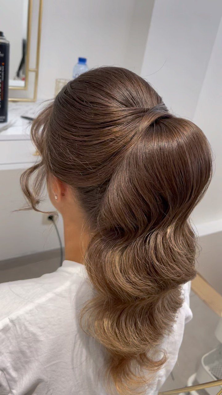 Curled brown ponytail with caramel balayage ends in a bright salon