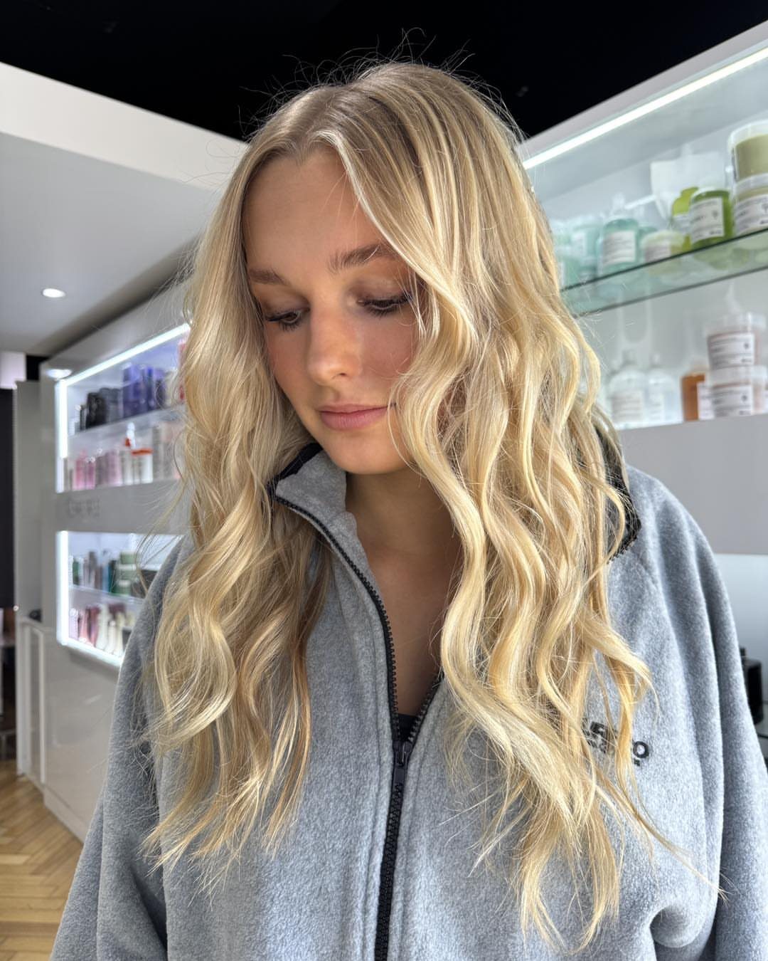 Woman with long, wavy blonde hair and darker roots in a salon