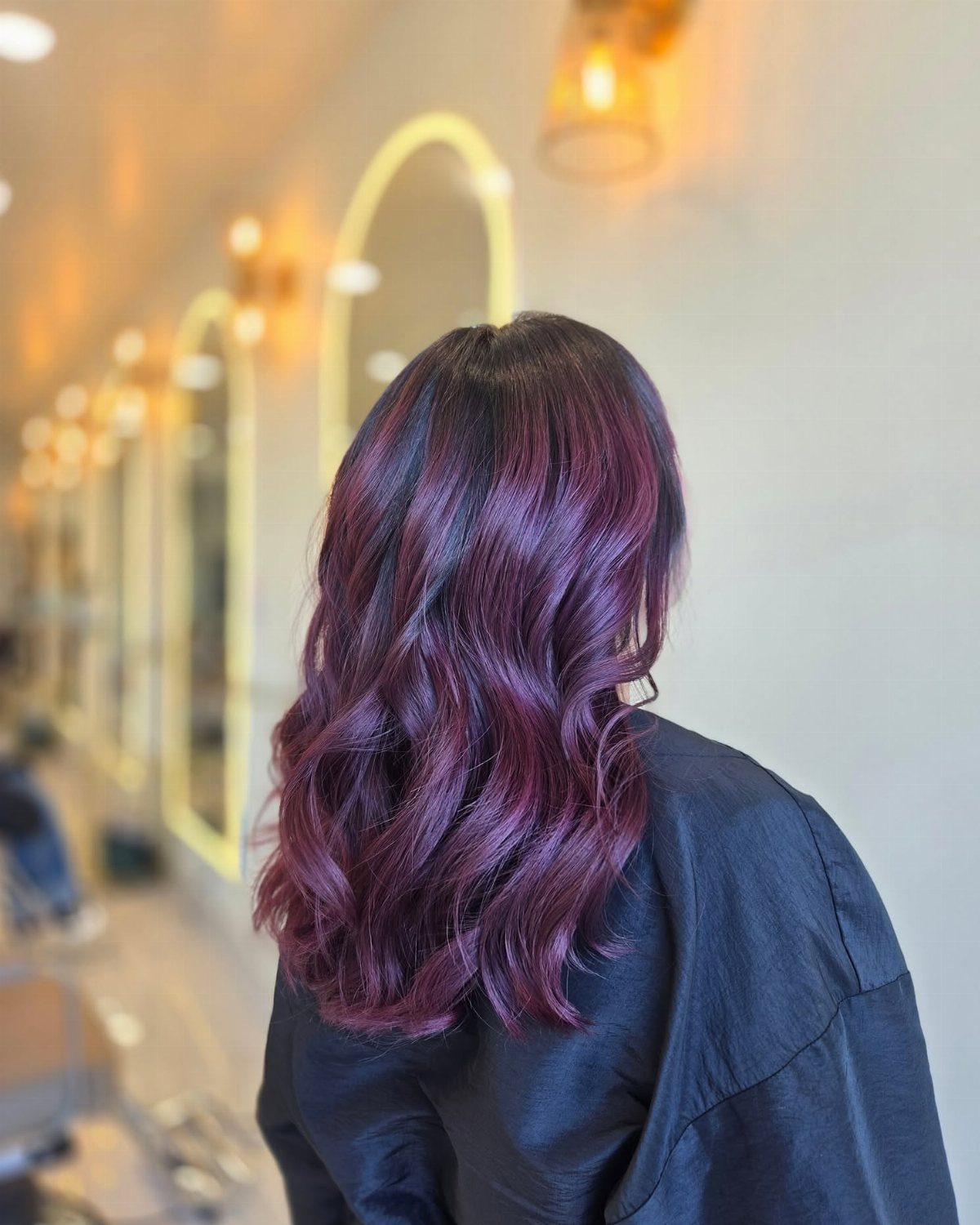 Wavy brunette hair with vivid burgundy coloring shown from behind in a salon