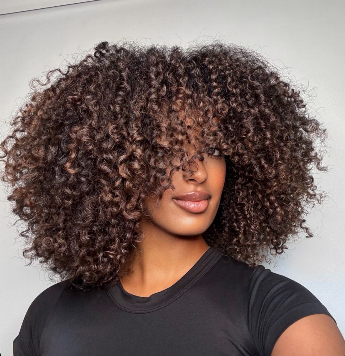 Woman wearing voluminous brown coils with subtle lighter painted highlights