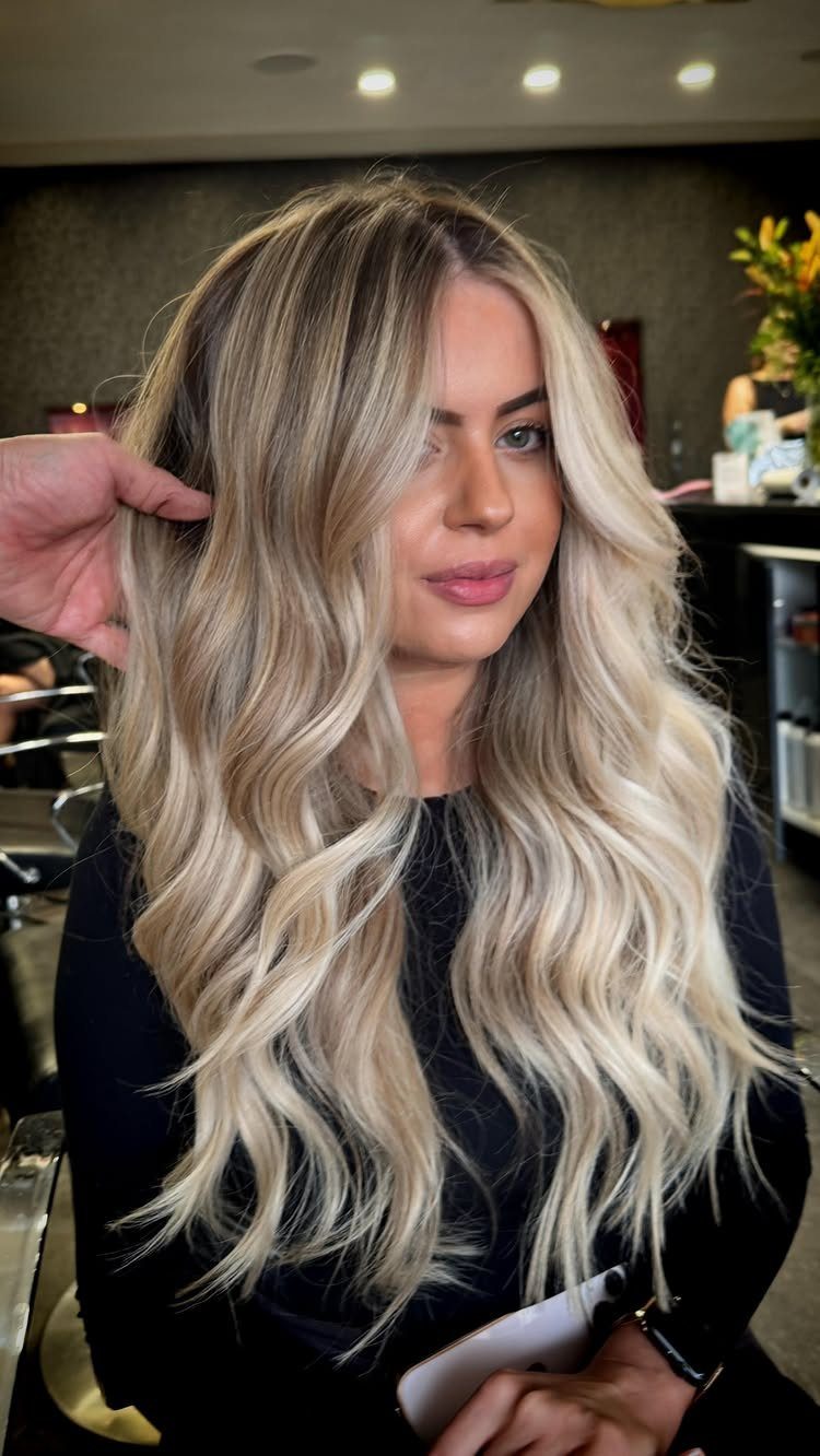 Woman displaying wavy blonde hair with dark roots in a salon chair