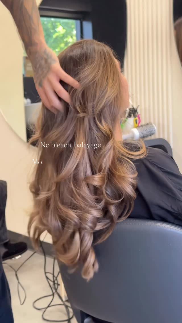 Long curled brown hair with subtle balayage, touched by a stylist in a salon