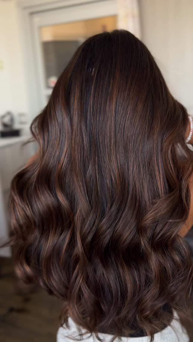 Long dark brown hair with subtle cinnamon highlights styled in loose waves