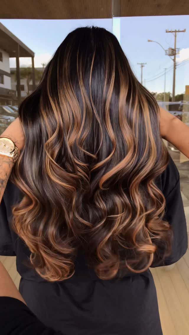 Long dark brown waves with caramel highlights against an outdoor street background