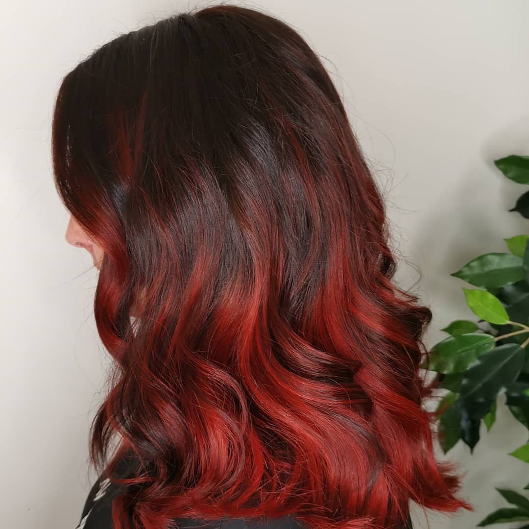 Dark brown curls with chunky red highlights against a pale wall