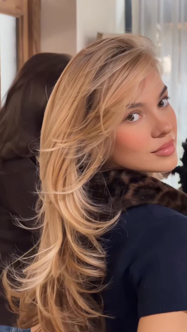 Woman showing long layered brown hair with golden highlights in a salon chair