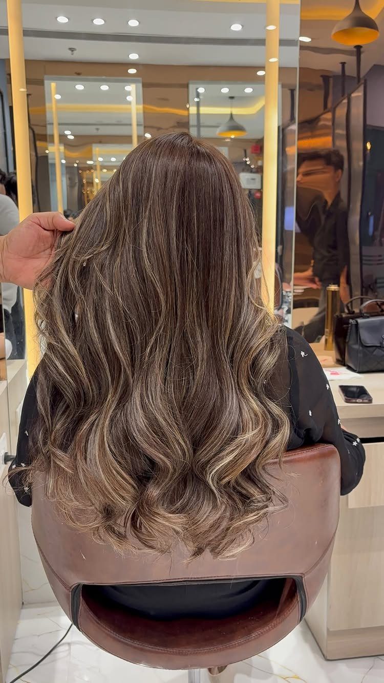 Wavy mushroom brown hair with subtle ash and taupe highlights in a salon