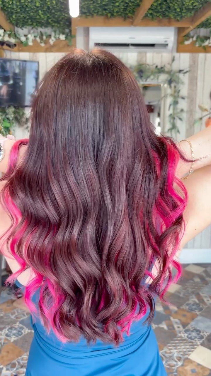 Long dark brown waves feature bright pink highlights in a salon