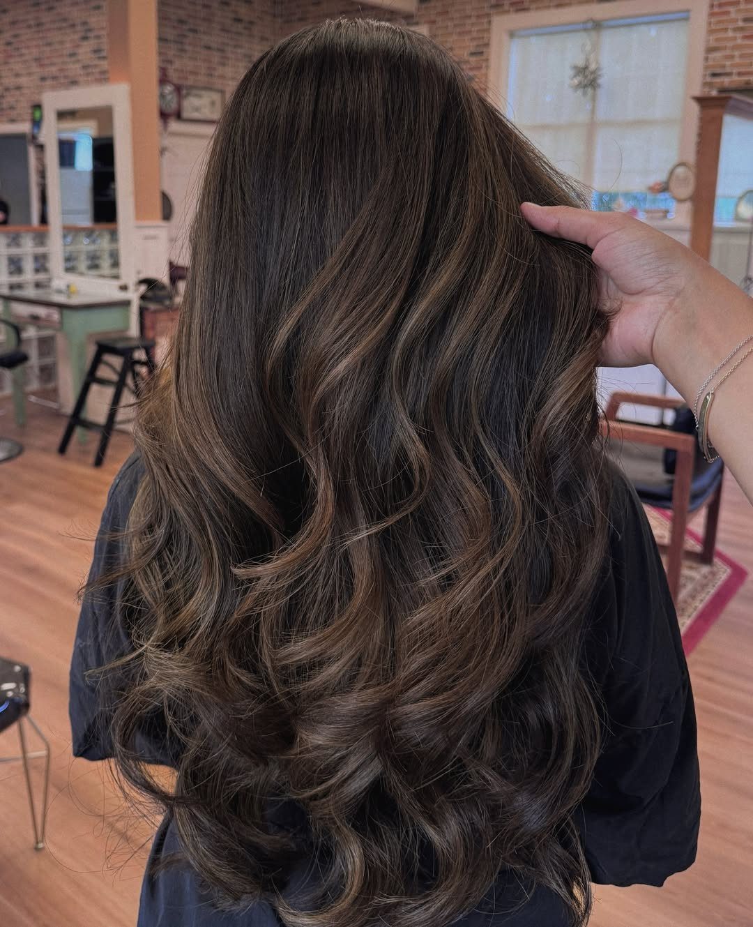 Long dark brown hair with subtle highlights styled in loose waves