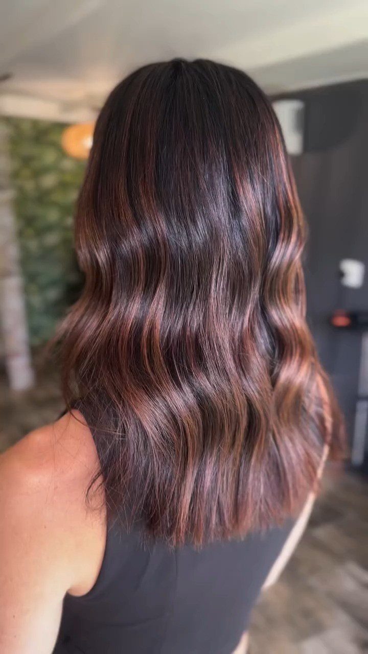 Long wavy brown hair with subtle auburn-red highlights in a salon