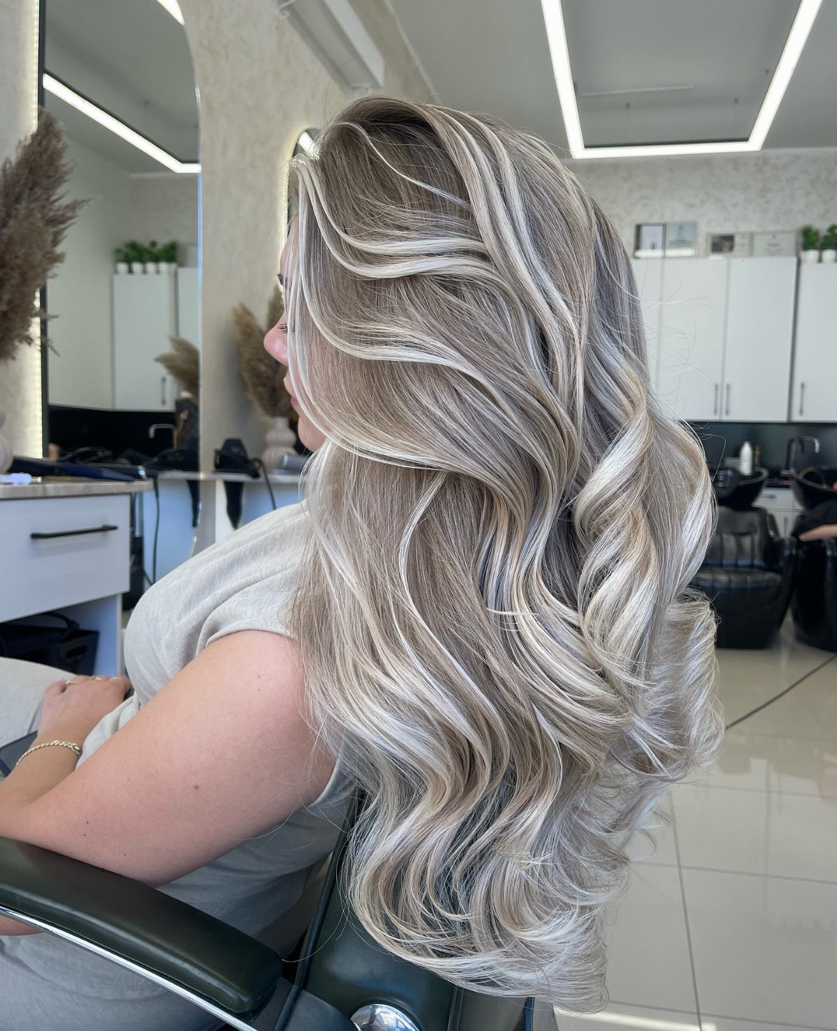 Long platinum balayage curls with a dark root shadow in a salon