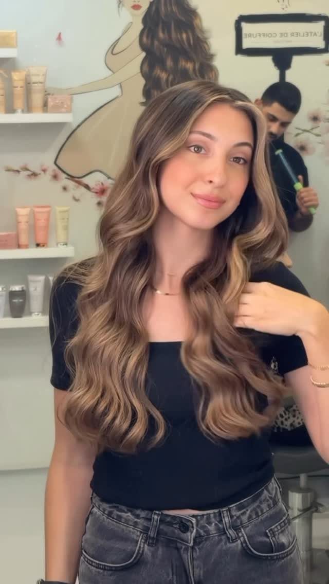 Woman poses in a salon with long wavy brown hair and caramel highlights
