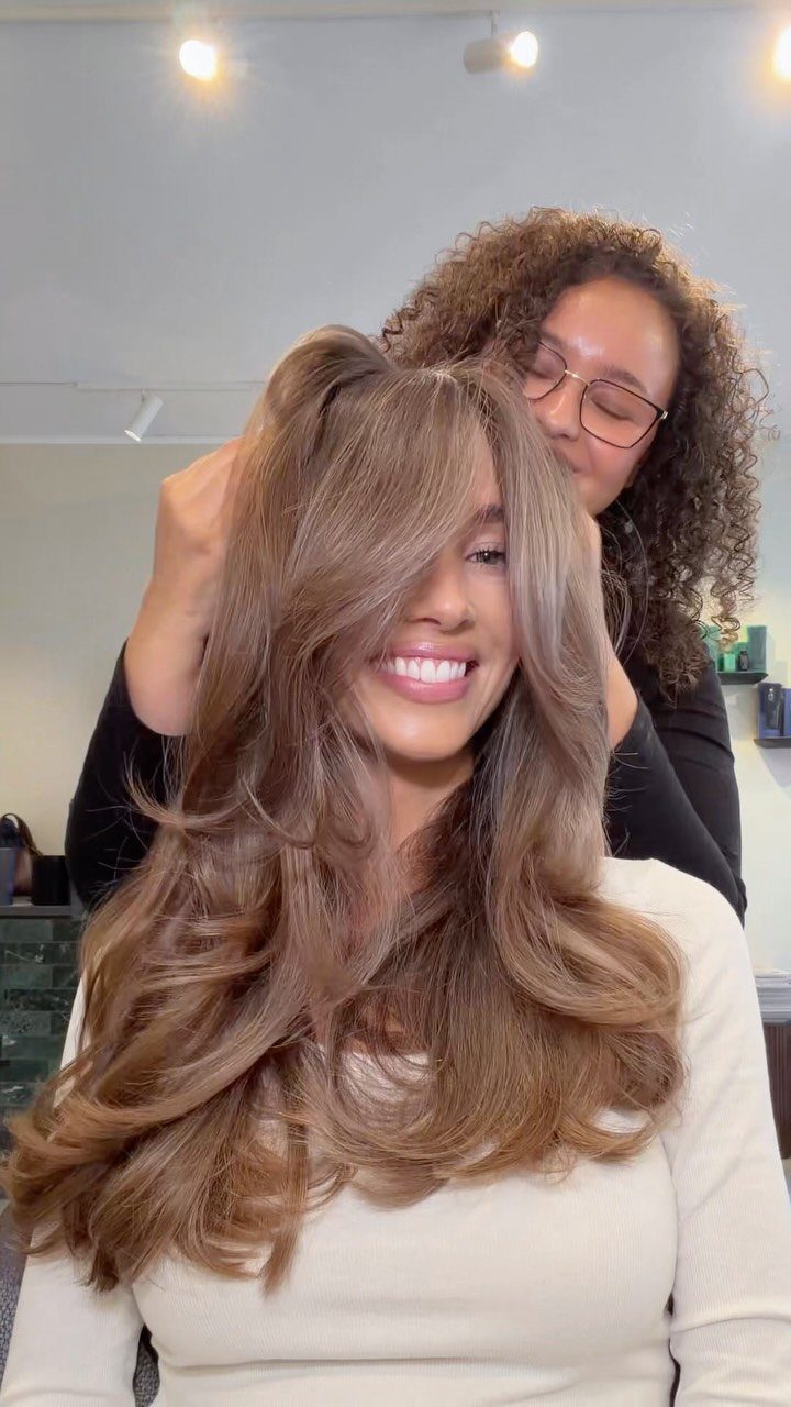 Woman showing long, layered brown hair with warm honey-blonde highlights in a salon