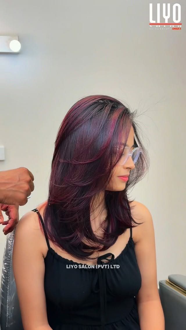 Woman with layered dark hair and vivid red highlights seated in a salon