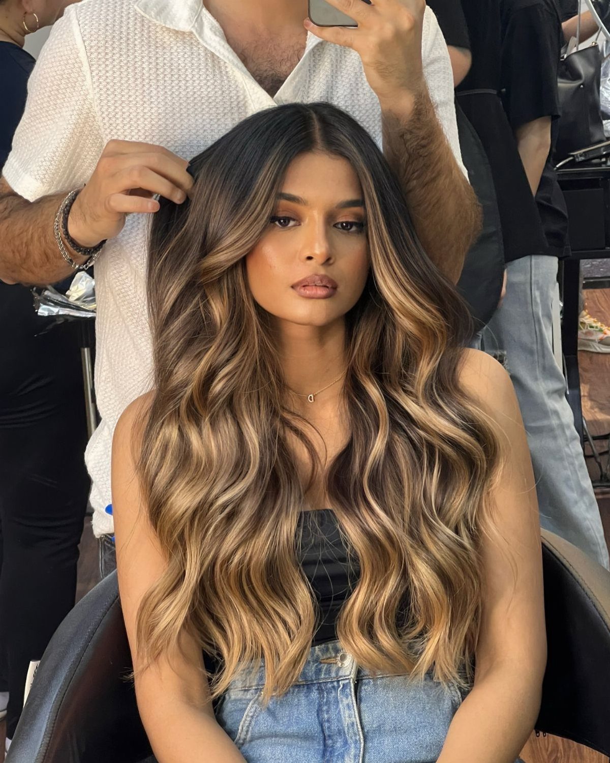 Woman displaying long, wavy brown hair with blended caramel highlights in a salon