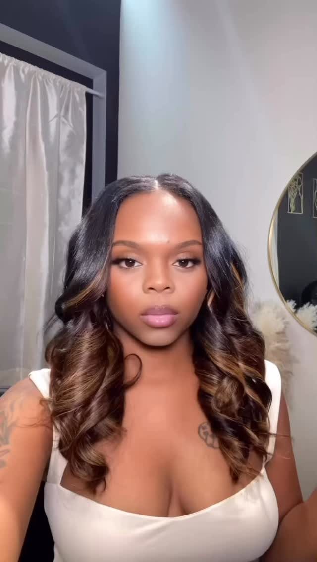 Woman with long, curled chocolate brown hair and lighter balayage highlights