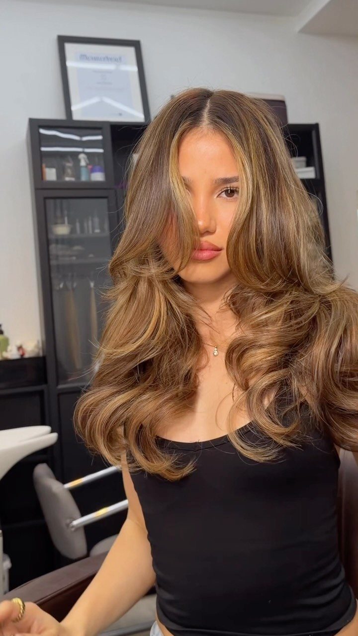 Woman showing voluminous layered brown hair with broad caramel highlights and loose curls