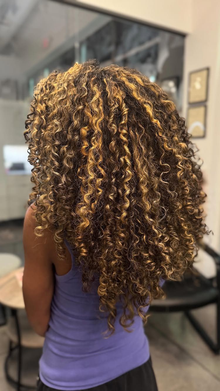 Long brown curls with honey-blonde highlights shown from behind in a salon
