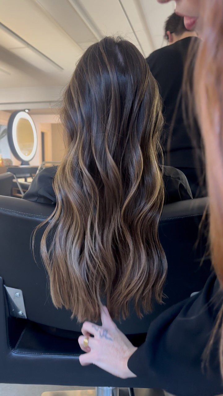 Long wavy dark hair with blended golden blonde and caramel highlights in salon