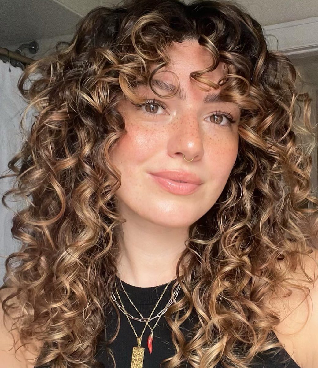 Woman with long curly brown hair and golden highlights framing her face