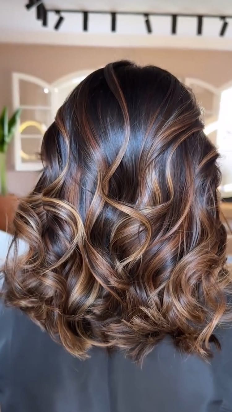 Mid-length dark brown hair with golden highlights styled in loose waves