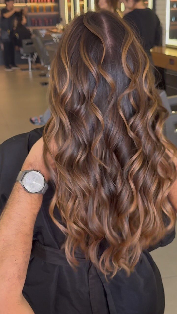 Long glossy brown waves with luminous caramel highlights in a salon