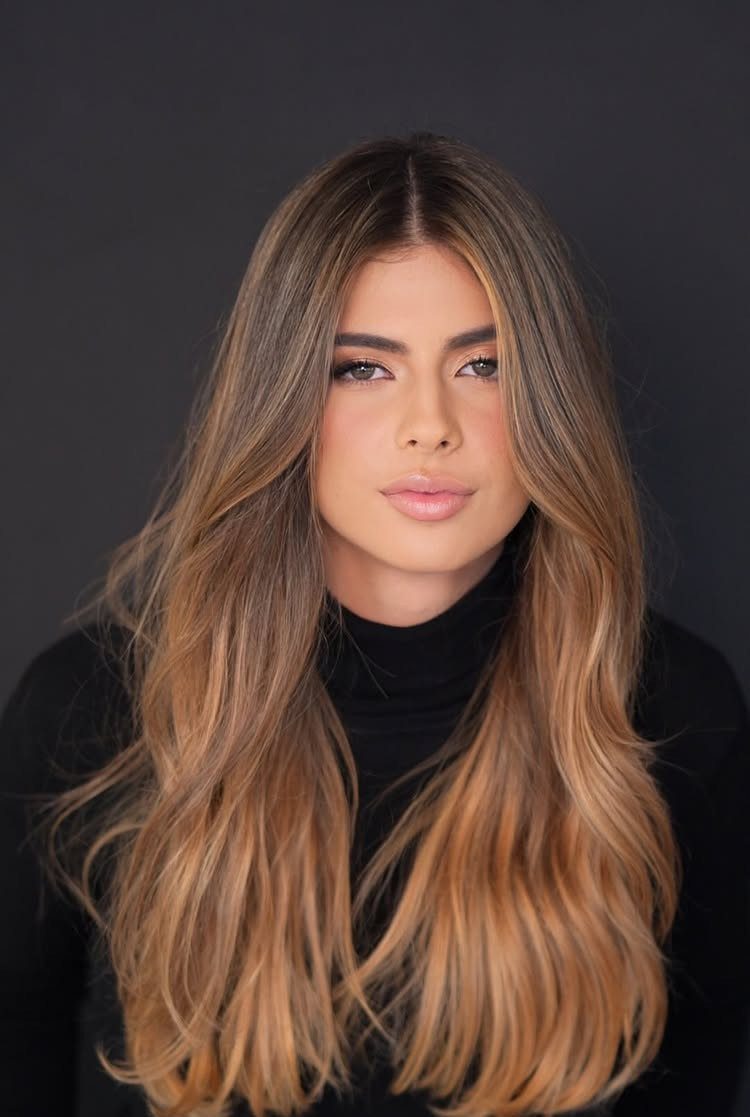 Woman with long wavy brown hair and warm honey highlights framing her face