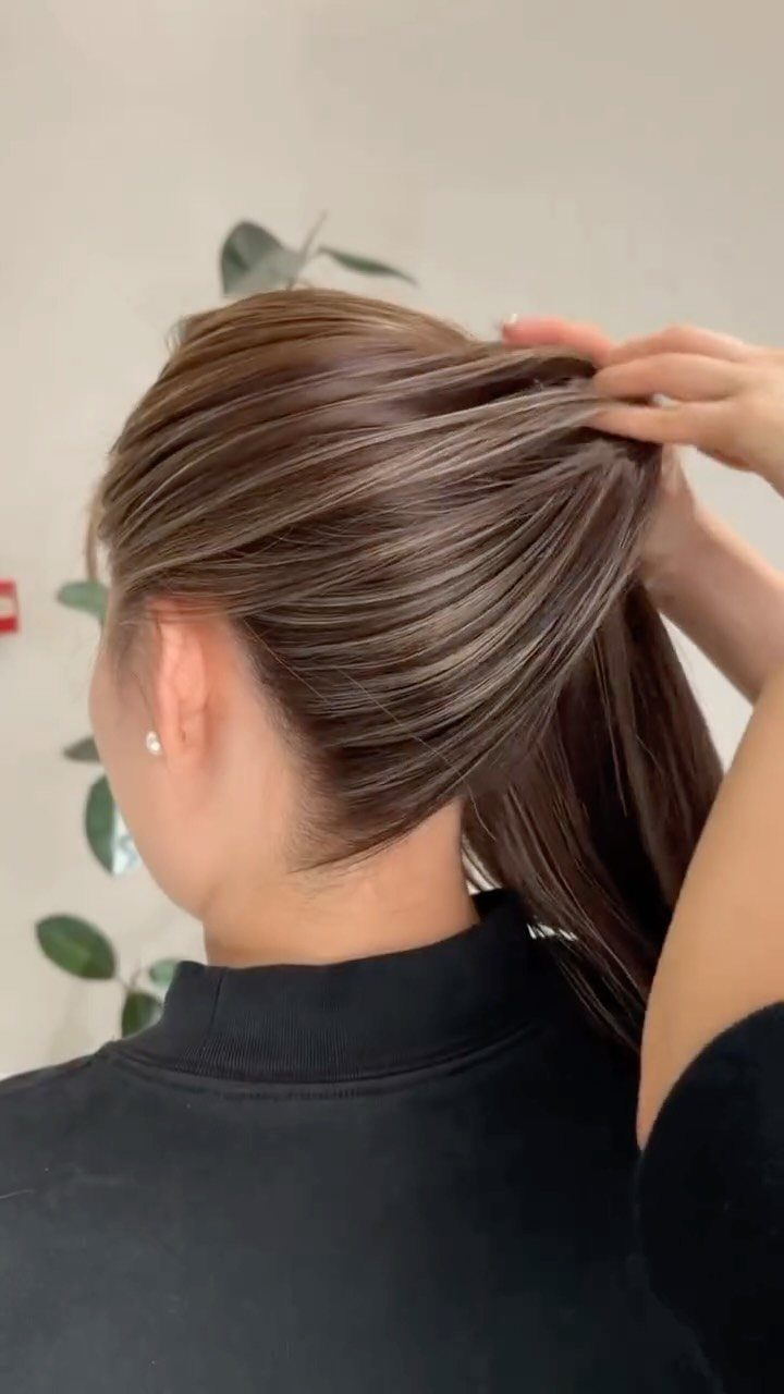 Fine light brown highlights blend through straight hair pulled back by hand