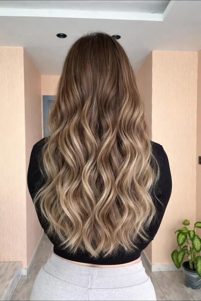 Long wavy brown hair blends into lighter blonde ends in graduated highlights