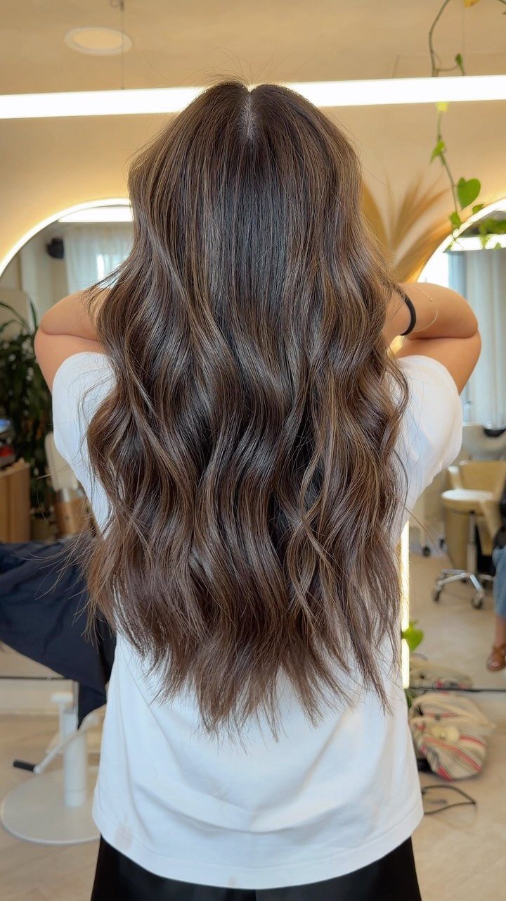 Long wavy dark brown hair with subtle light brown highlights in a salon