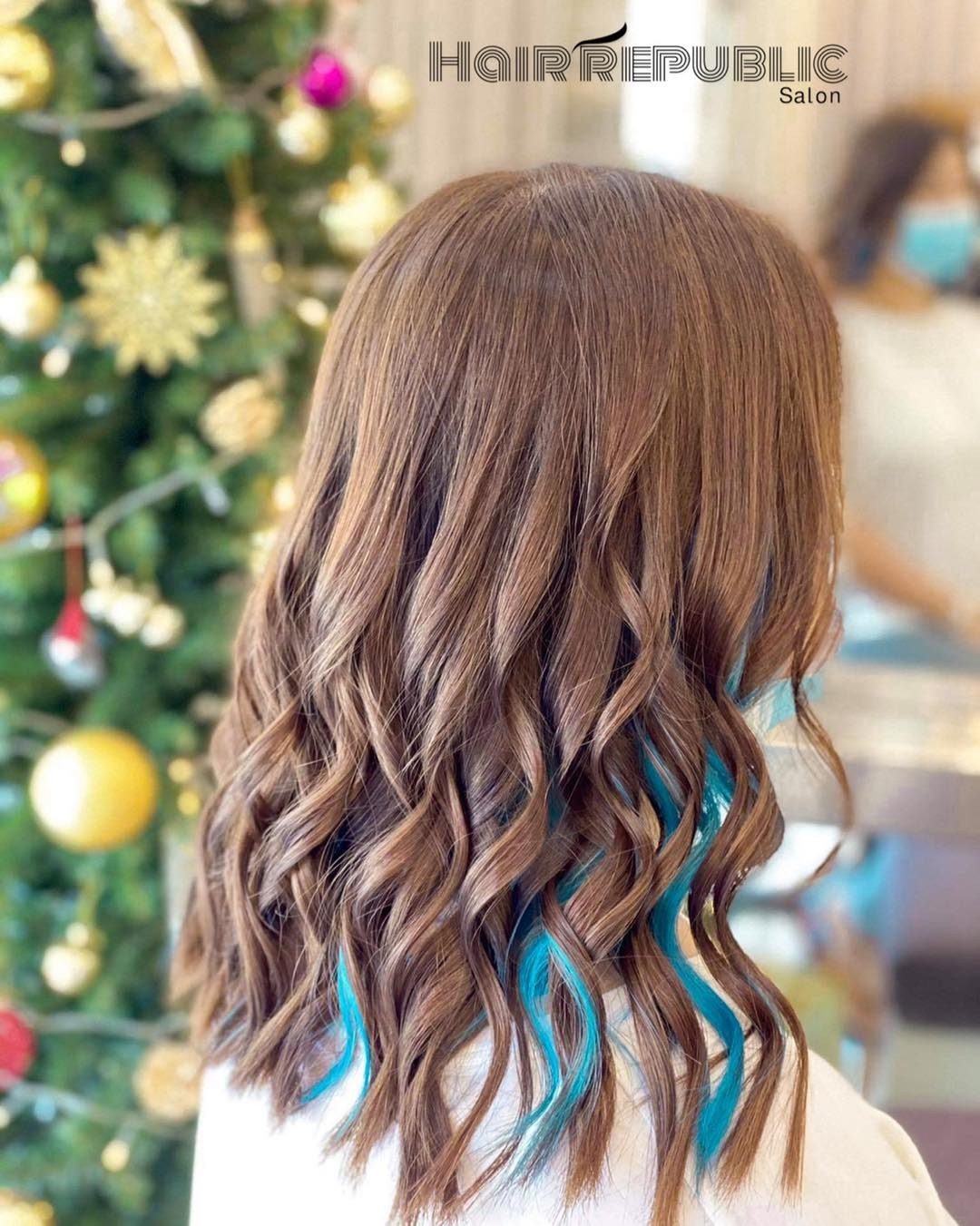 Wavy light brown hair with bright blue highlights woven through the ends
