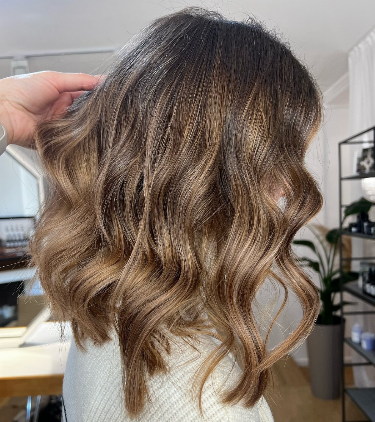 Wavy brown hair with warm caramel highlights shown from behind in a salon