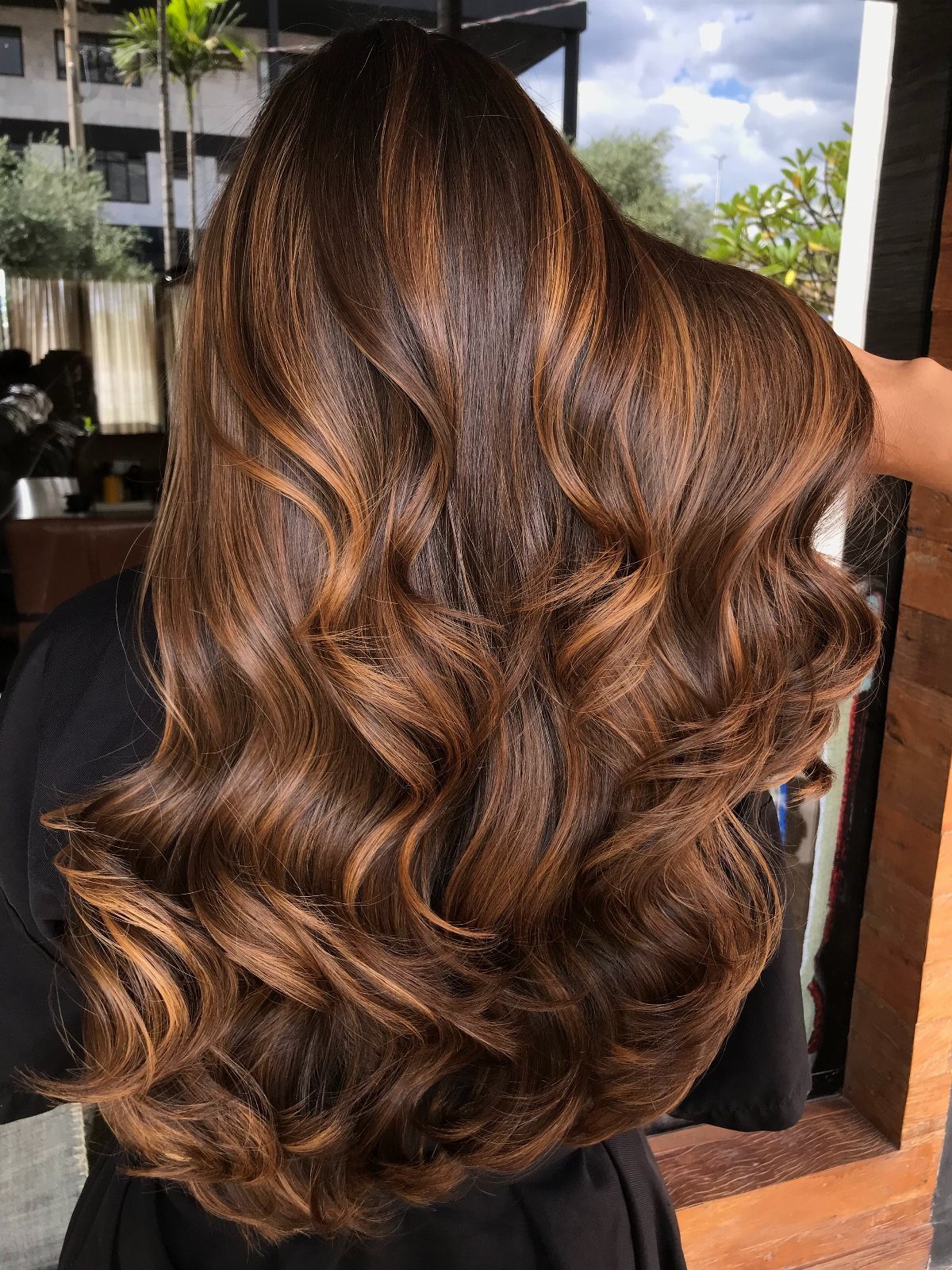 Long brunette curls show warm honey highlights throughout the hair