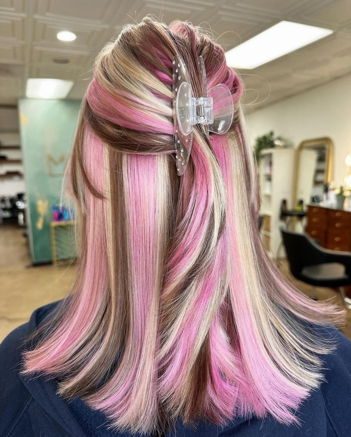 Long layered hair displays alternating pink, blonde, and taupe highlights in a salon.