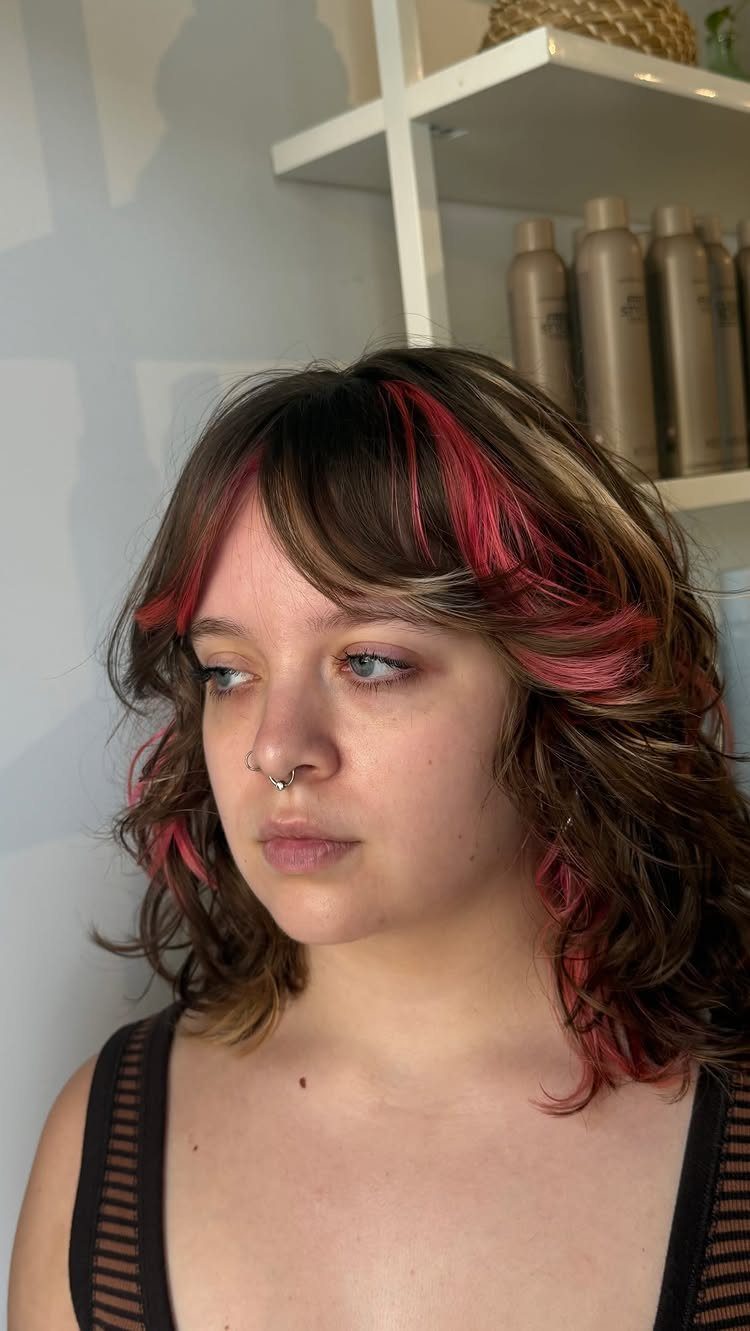 Person with wavy brown hair and vivid pink face-framing highlights indoors