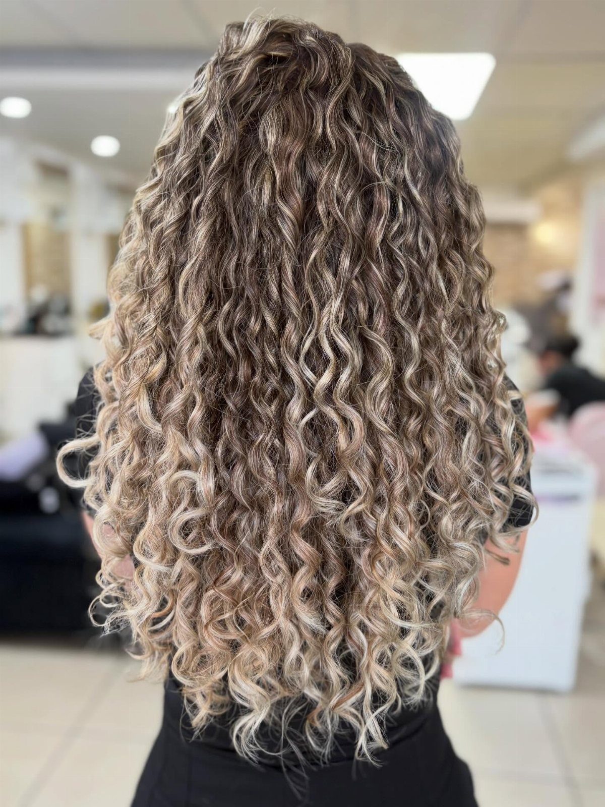 Curly hair with dark roots and light blonde highlights in a salon