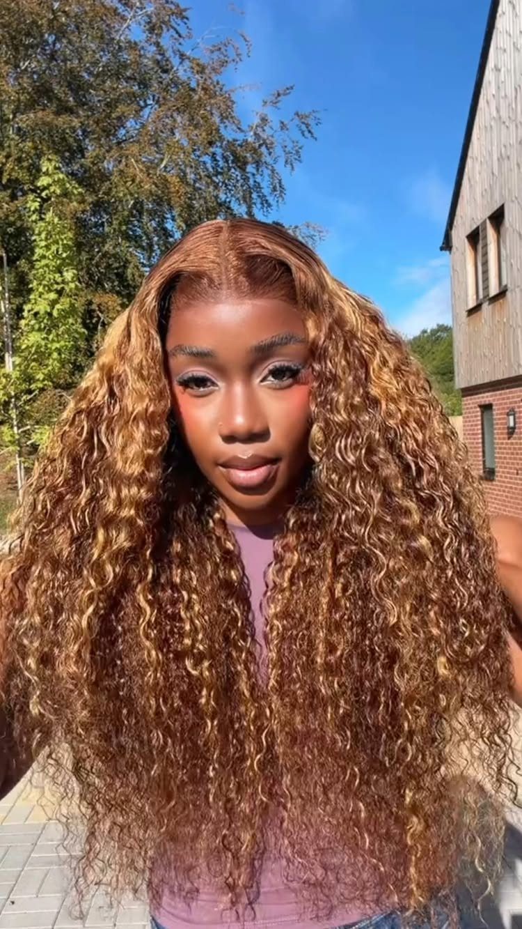 Woman showcasing long curly brown hair with warm honey-blonde highlights outdoors