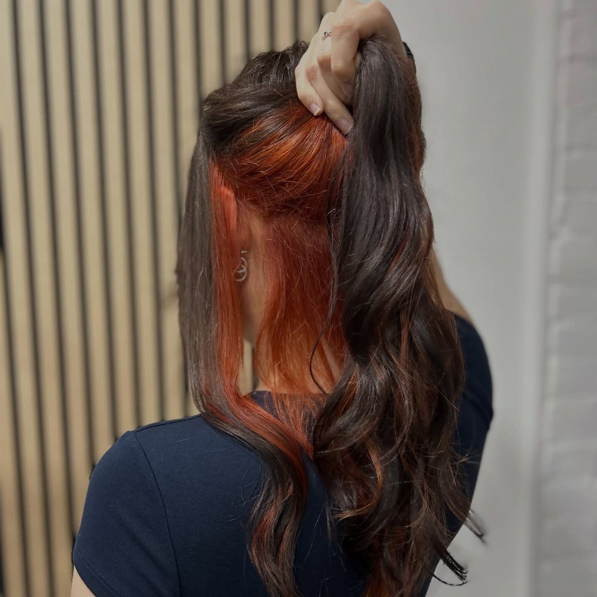 Dark wavy hair lifted to reveal vivid copper-red highlights underneath