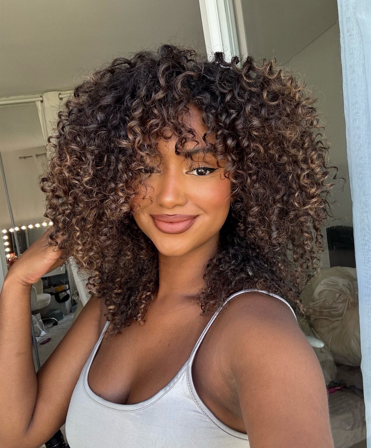 Woman with voluminous curly brown hair and subtle reddish-brown highlights posing indoors