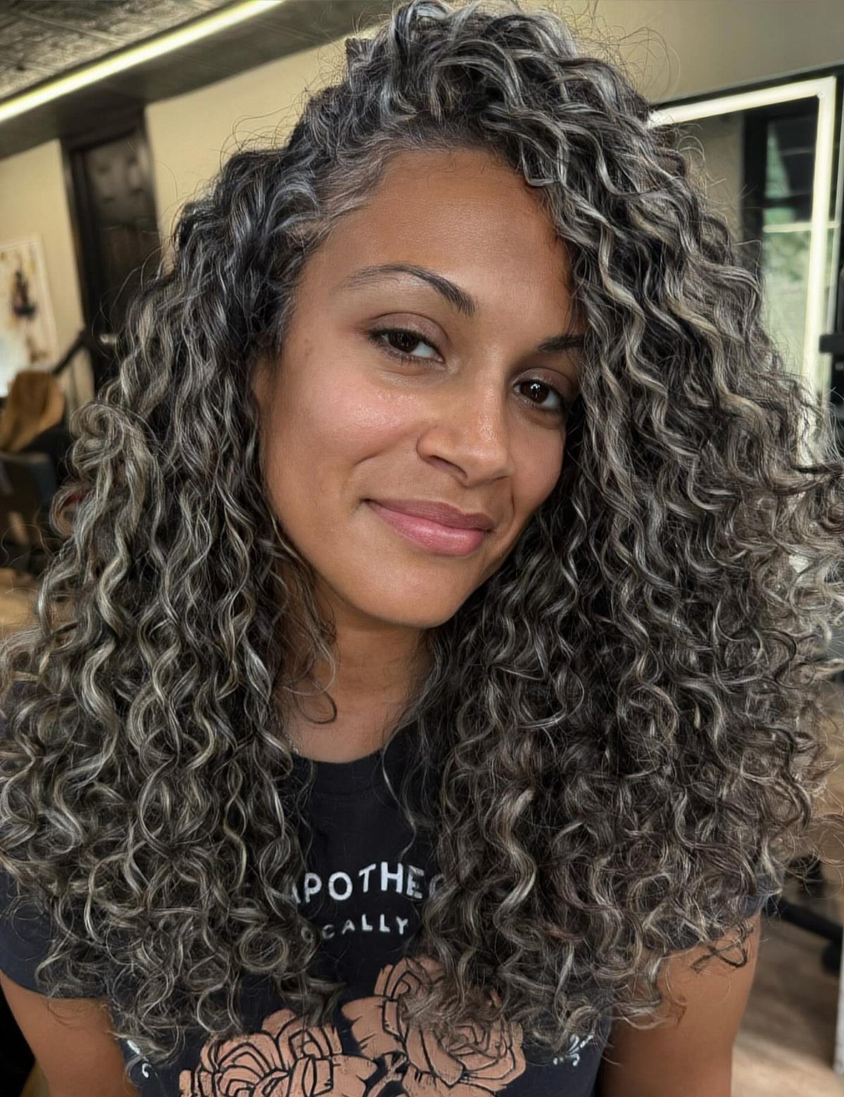 Woman showing long dark curls with silver-gray highlights in a salon