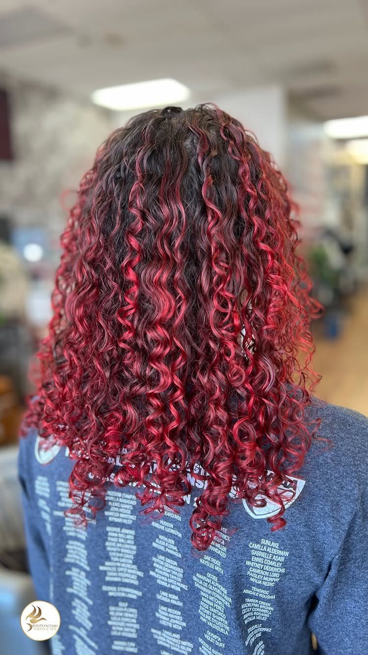 Long dark curls with vivid red highlights cascading over a blue printed shirt