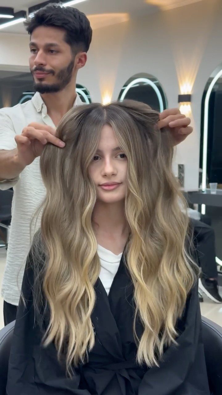 Woman with long, wavy blonde balayage hair seated in a salon