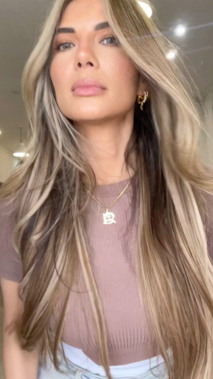 Woman showing long wavy bronde hair with dark roots and blonde highlights