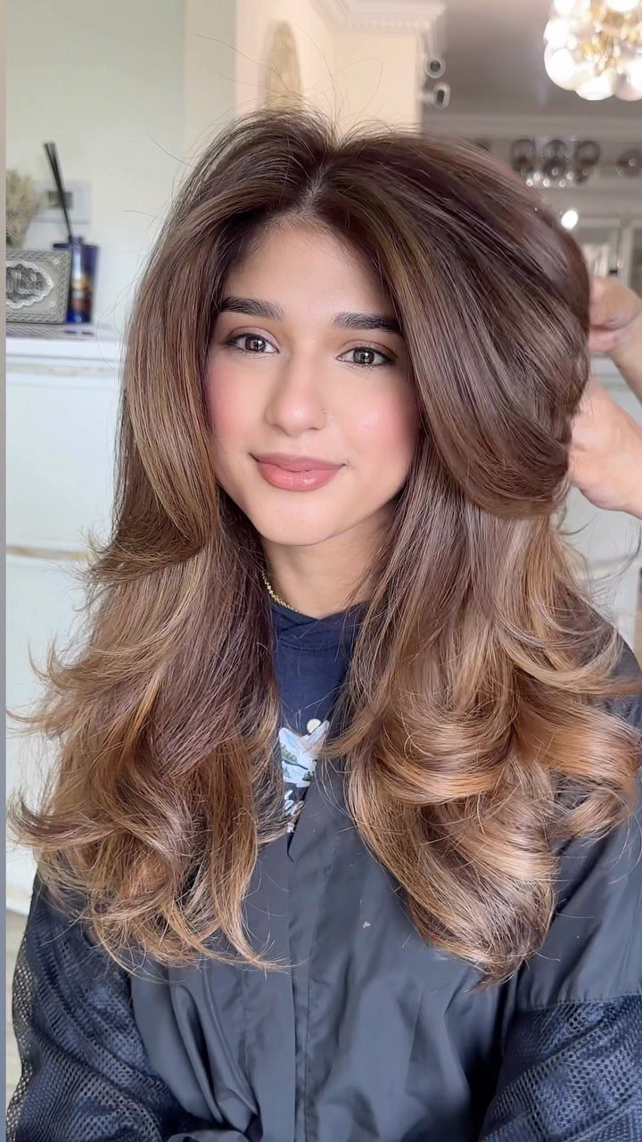 Woman showing long wavy brown hair with warm caramel blonde highlights in a salon
